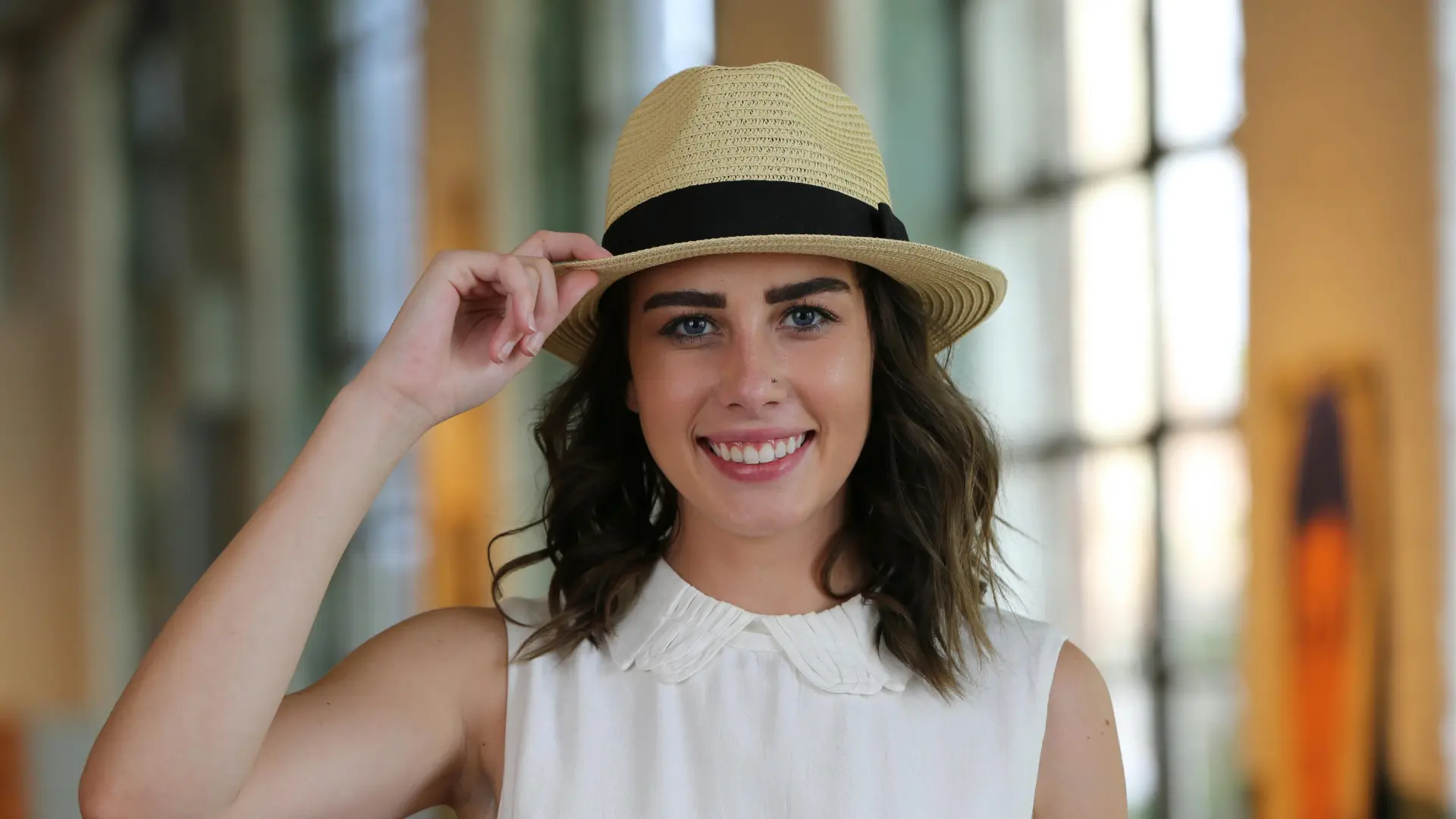 A smiling, happy woman holding the brim of her hat